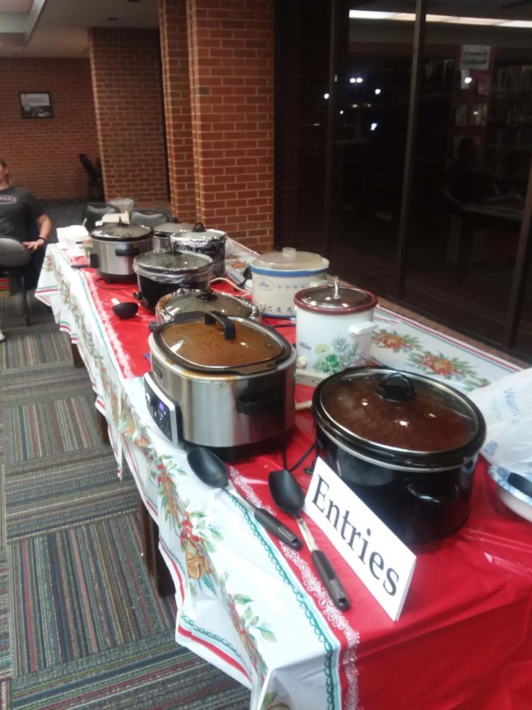 A table with eight crock pots of chili and sign that says entries 